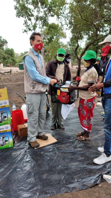 Um membro da comunidade recebe das mãos de Chance Briggs uma motobomba como parte do apoio do desenvolvimento agrícola em Dombe
